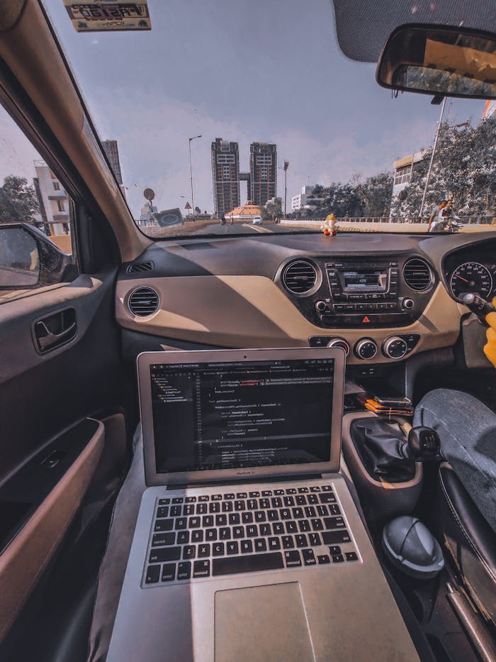 ours-journey Car interior with laptop on dashboard, city view outside, sunny day.